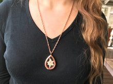 A young woman with long brown hair and black shirt wears a long locket necklace. The locket necklace is rose gold and made of glass and metal. It is see-through. Inside the see-through pendant is a single white pressed edelweiss flower. The edelweiss locket is available for sale, handmade by Pressed Wishes. 
