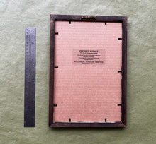 The back of a handmade picture are shown with a ruler to the left side and a sticker to describe the flower and name the artisan. 