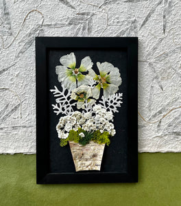 A Bouquet of pressed flowers including Hollyhock, Pearly Everlasting, and moss are contained in a birch planter pot and framed with a wooden frame. The pressed botanical artwork is by Pressed Wishes.