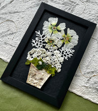 A Bouquet of pressed flowers including Hollyhock, Pearly Everlasting, and moss are contained in a birch planter pot and framed with a wooden frame. The pressed botanical artwork is by Pressed Wishes.
