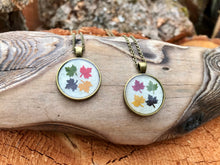 4 different coloured (red, yellow, green, black) real pressed Maple leaves arranged on a white resin background in a zinc alloy antique bronze pedant. Each pendant is sealed with an eco friendly resin and handmade by Pressed Wishes.