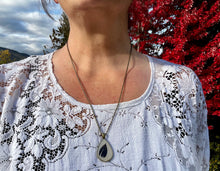 A model wears a raven feather pendant necklace. The pendant is handmade in Canada by Pressed Wishes. 