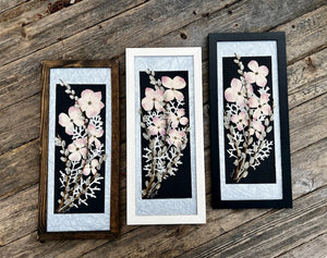 Pressed flowers are arranged in a floral bouquet containing pink dogwood, pussy willow and musk mallow. The floral bouquet is framed and available to hang on the wall as wall art. Handmade by Pressed Wishes.