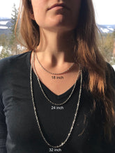 a young woman with long brown hair and a black shirt wears 3 different necklace chains. Each chain is a different length. Each chain is labeled with its length. 